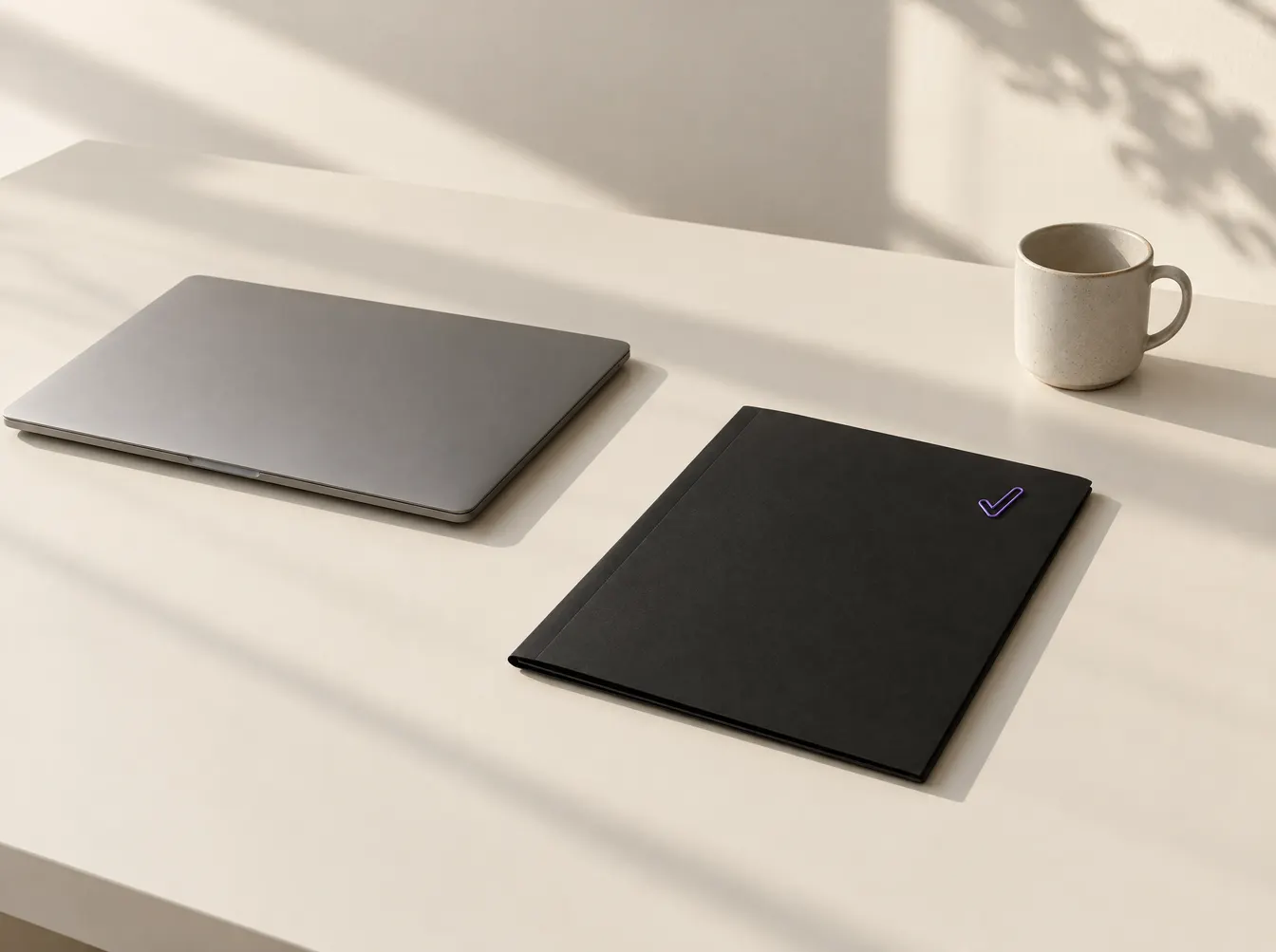 Aufgeräumter Schreibtisch mit geschlossenem Laptop, schwarzer Mappe mit violettem Häkchen und einer Tasse im Morgenlicht